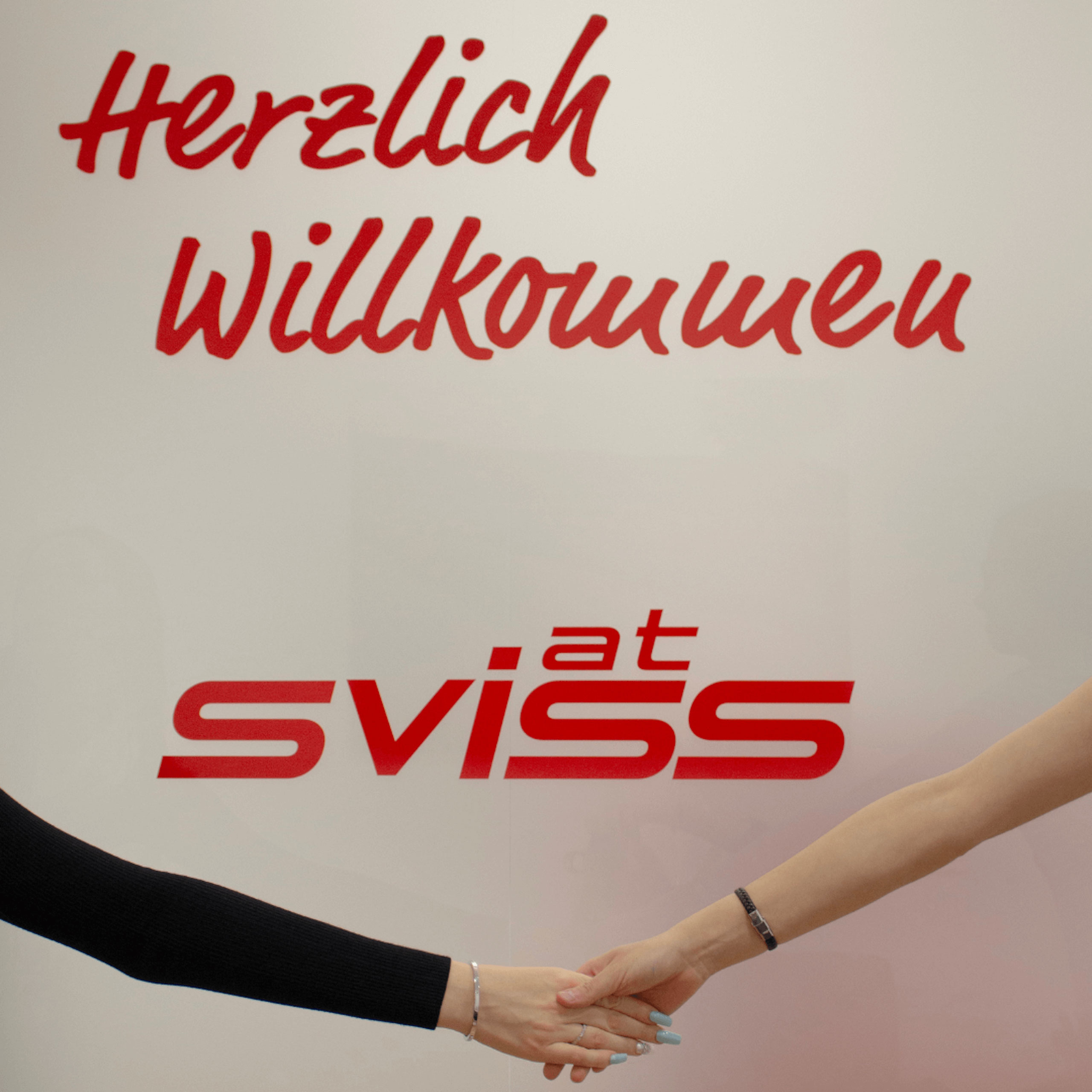 Personen schütteln sich die Hände vor einem Schriftzug "Herzlich Willkommen" und Sviss Logo